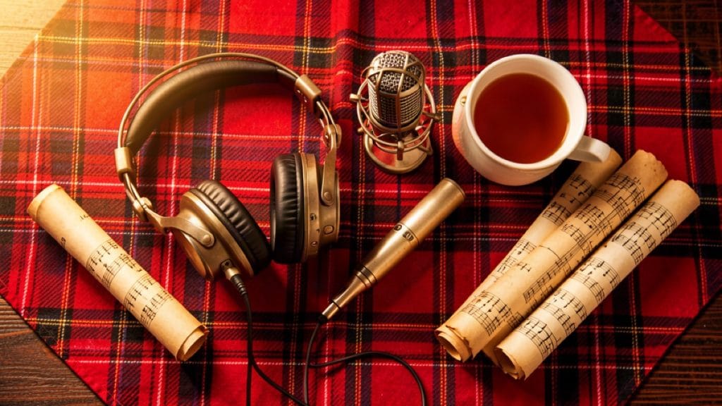 Flat-lay of headphones, a microphone, parchment scrolls and tea on a red and black tartan plaid