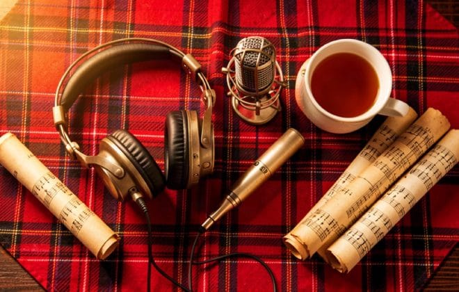 Flat-lay of headphones, a microphone, parchment scrolls and tea on a red and black tartan plaid