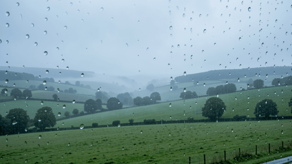 Soft Irish drizzle over a green valley with low mist and rain drops on a window